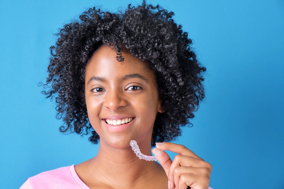 Smiling woman pointing to teeth against blue background for dental studio website.
