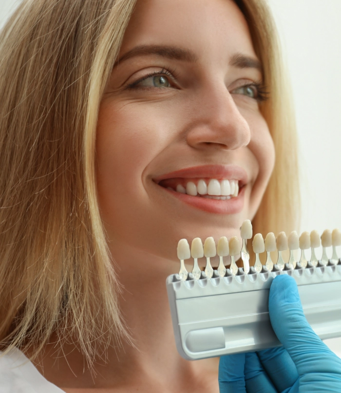 Woman smiling while dentist holds tooth shade guide for color matching during dental consultation.