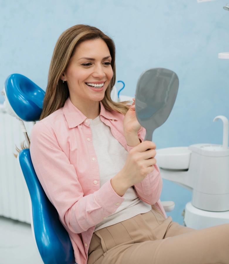 Woman in pink shirt holding dental mirror in bright dental office setting