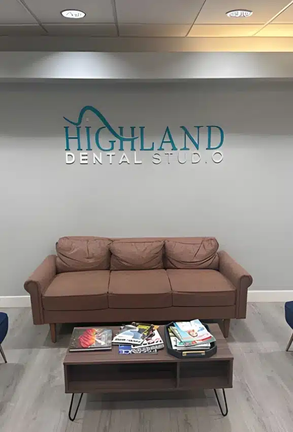 Highland Dental Studio waiting room with beige couch, coffee table, and logo on wall.
