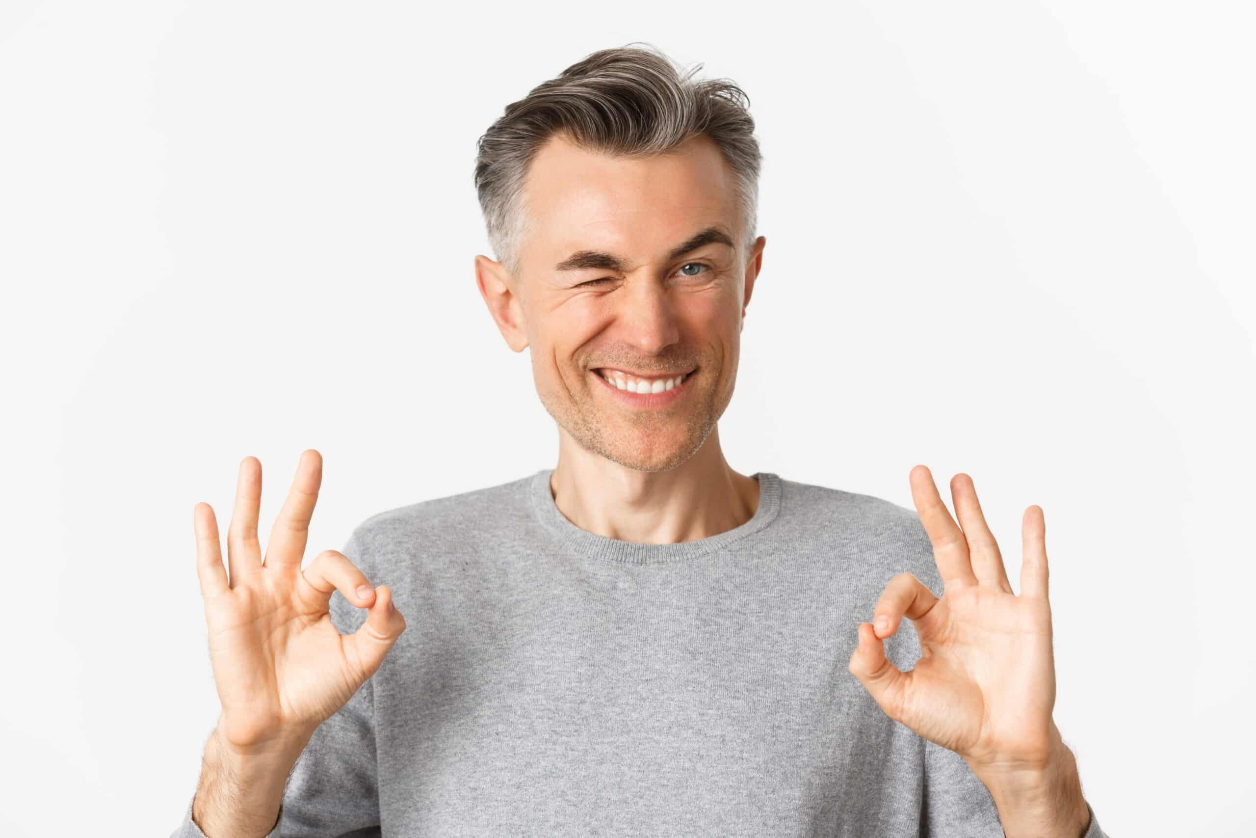 Man giving two thumbs up gesture, smiling at camera during dental implant recovery.
