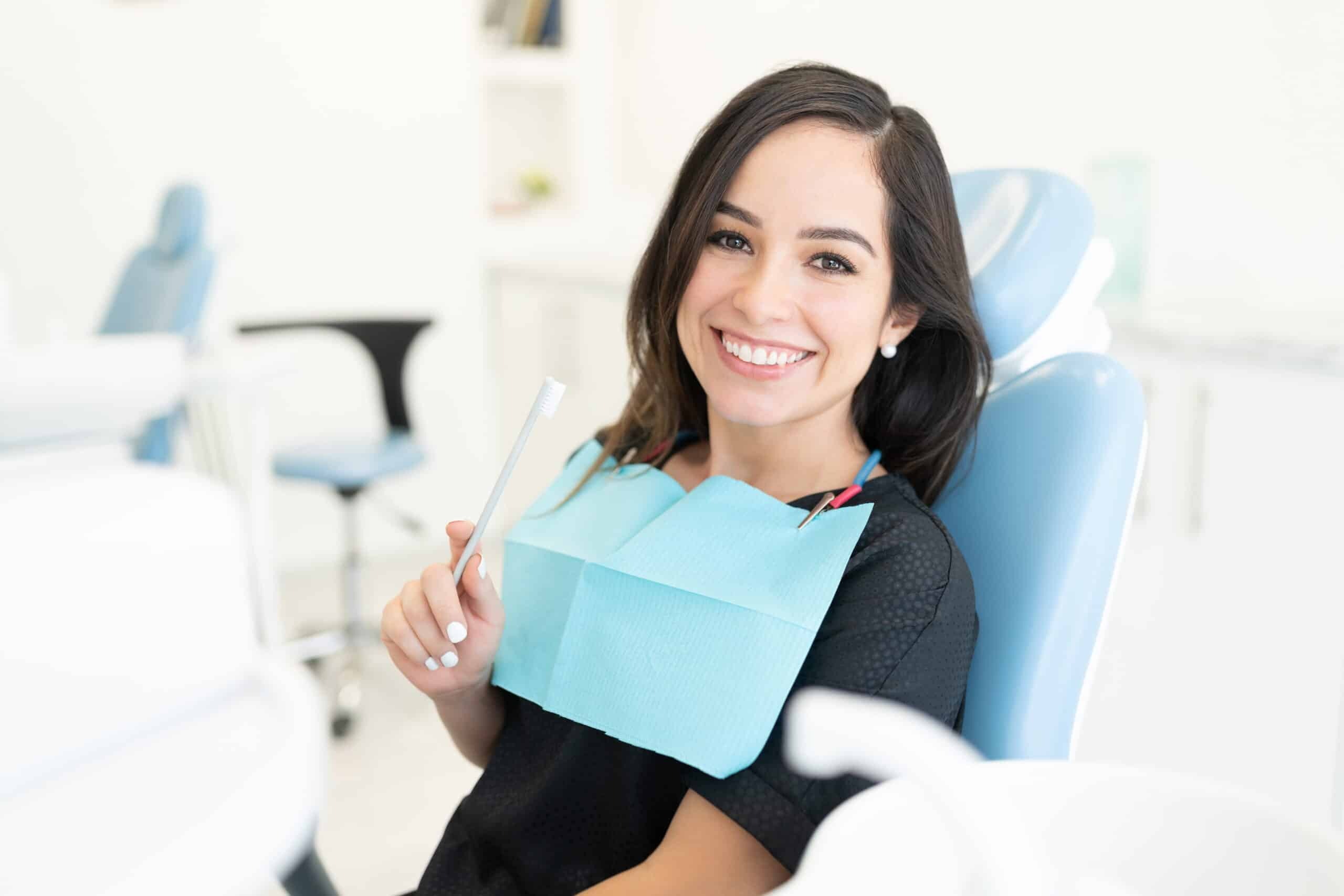 Smiling woman holding dental bib in modern dental office treatment room.