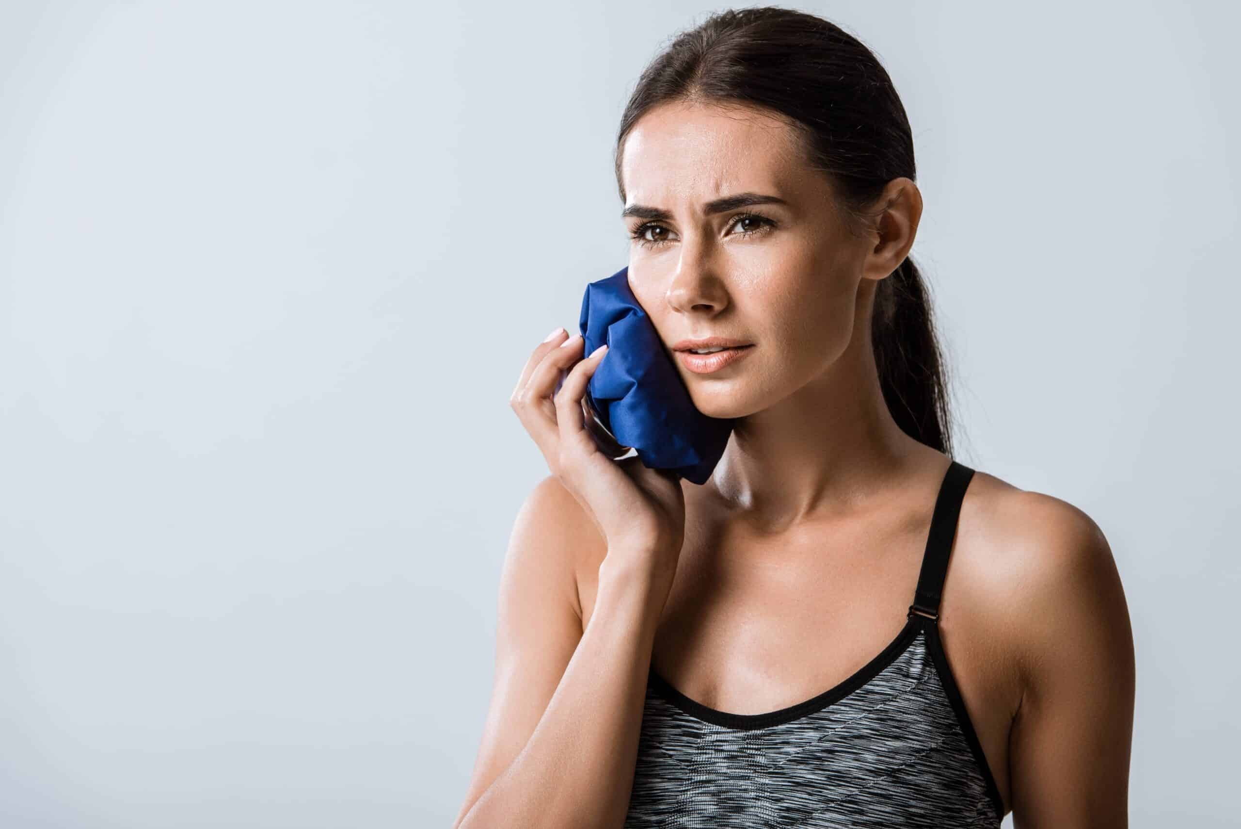 Woman applying ice pack to her cheek for post-filling tooth pain relief.